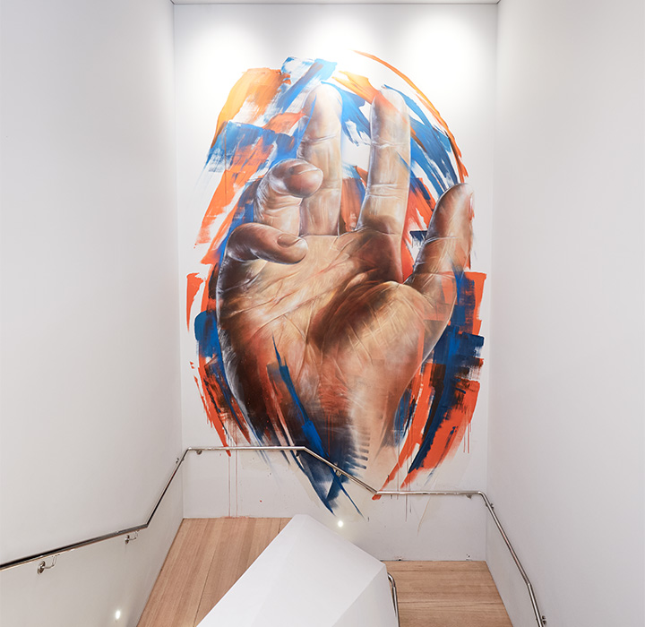 A painting of a hand with blue and orange brush strokes behind it